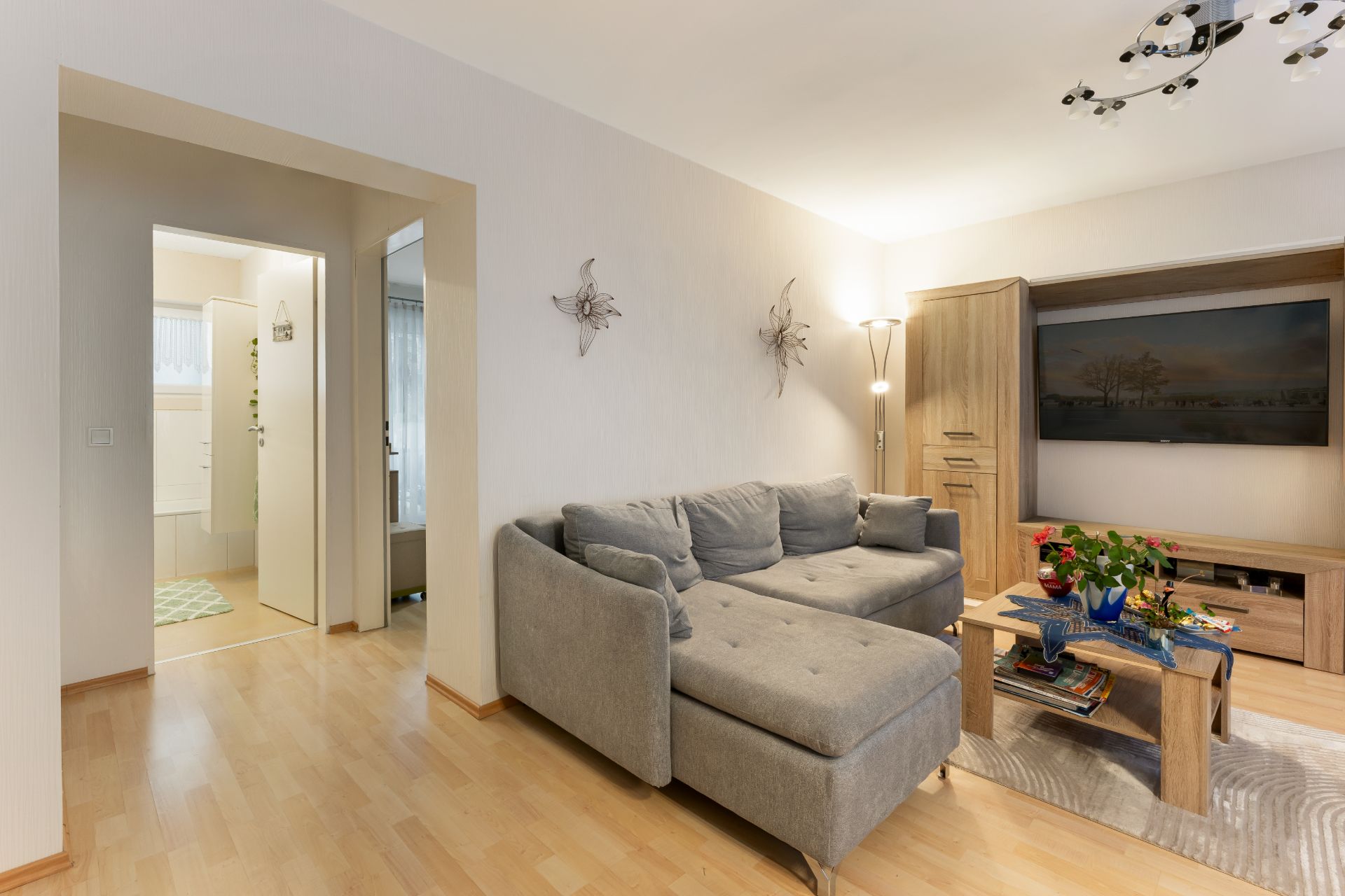 Wohnzimmer mit grauem Ecksofa, Couchtisch und Fernseher auf Holzschrank.