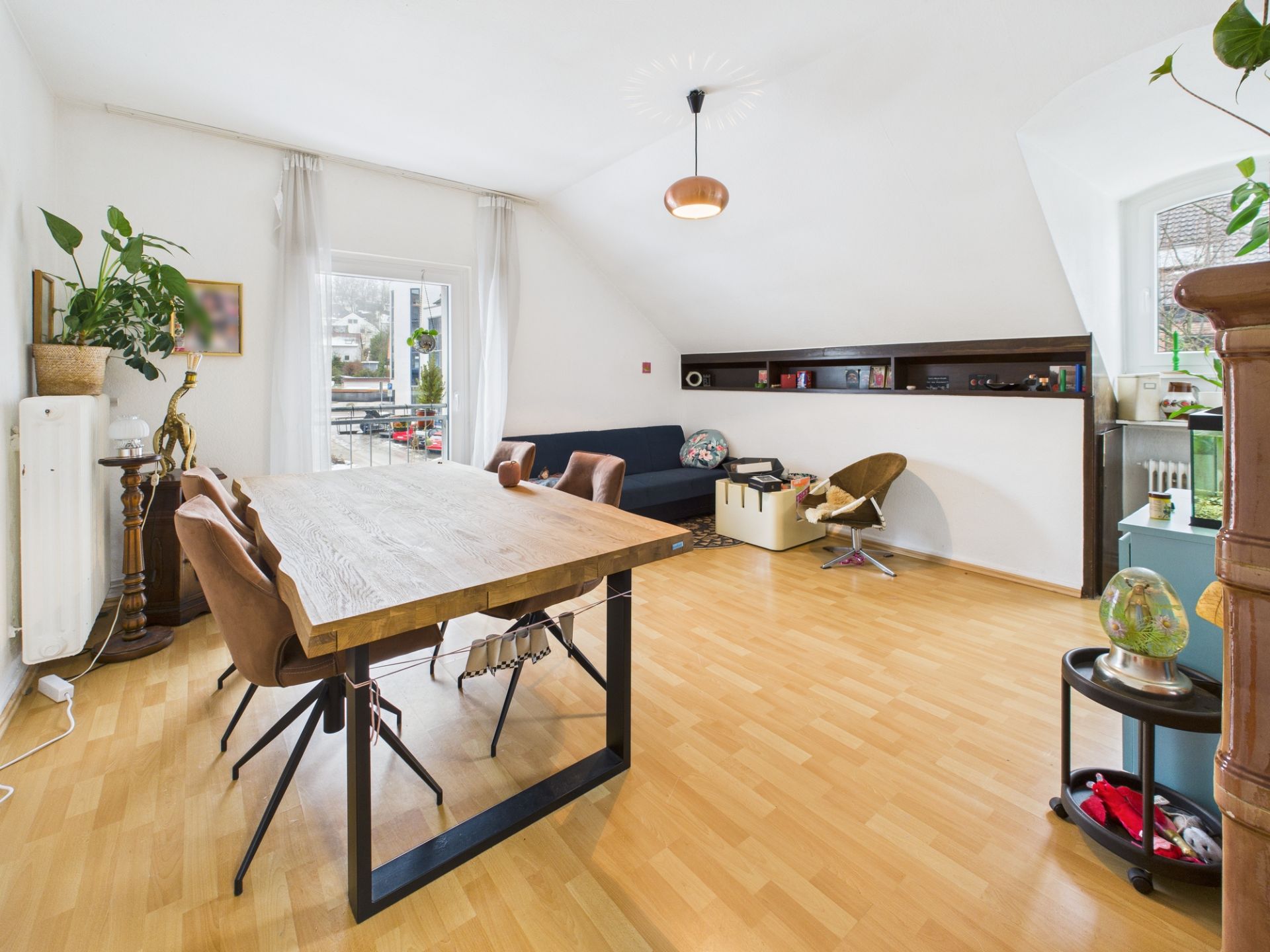 Helles Wohnzimmer mit Holzboden, Esstisch, Stühlen, Sofa und Regalen unter einer Dachschräge.