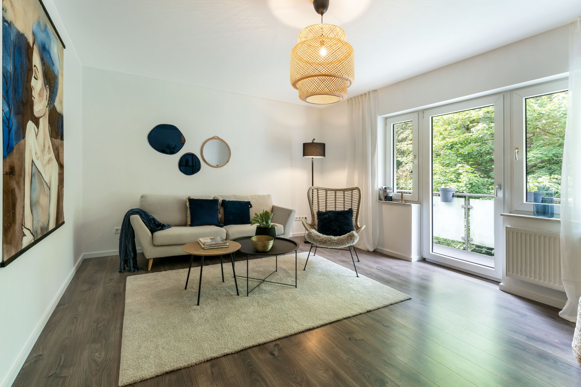 Helles Wohnzimmer mit Sofa, Teppich, Sesseln, Couchtischen und Zugang zum Balkon.