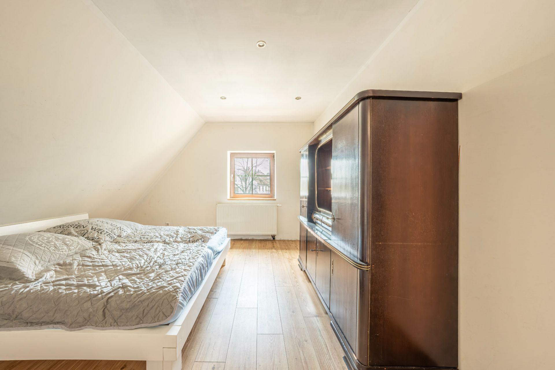 Helles Schlafzimmer mit Doppelbett, Holzschrankwand und Fenster, Holzboden.