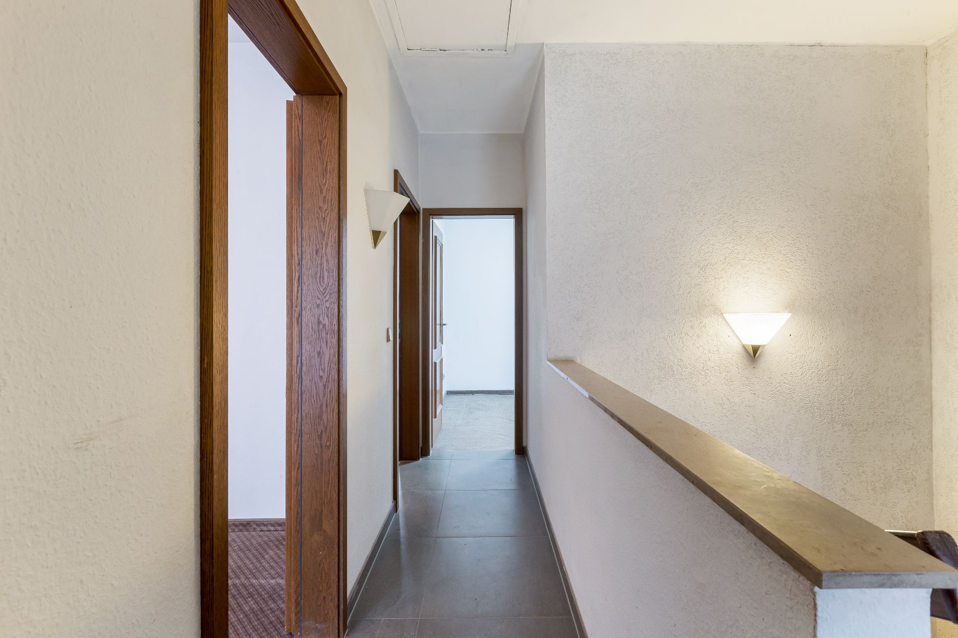 Heller Flur mit Fliesenboden, Holztüren und Wandlampe in einem Wohnhaus.