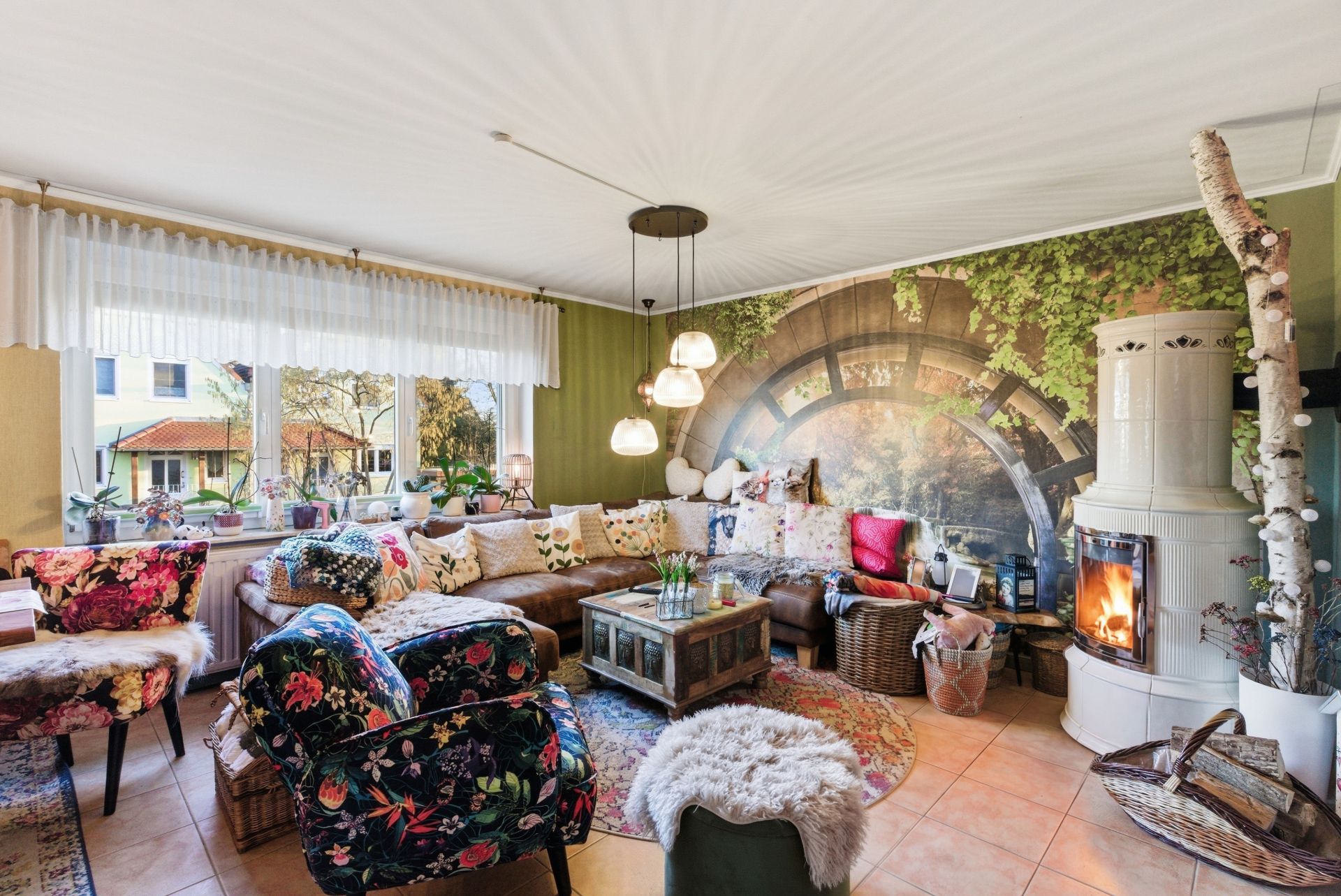 Gemütliches Wohnzimmer mit bunten Möbeln, Kaminofen, Pflanzen und großer Fensterfront.