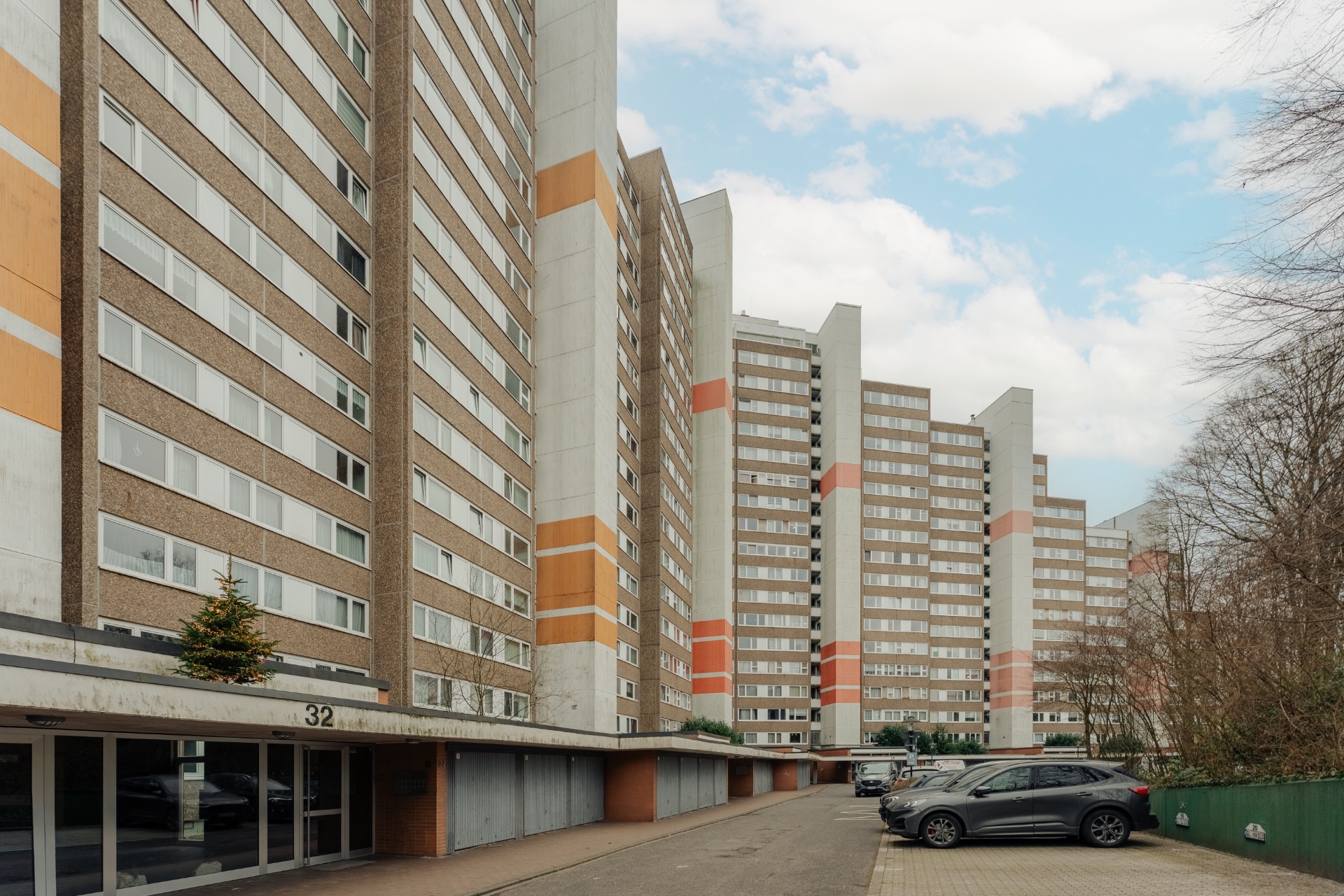 Mehrstöckige Wohngebäude mit orangefarbenen Streifen und geparkten Autos davor.