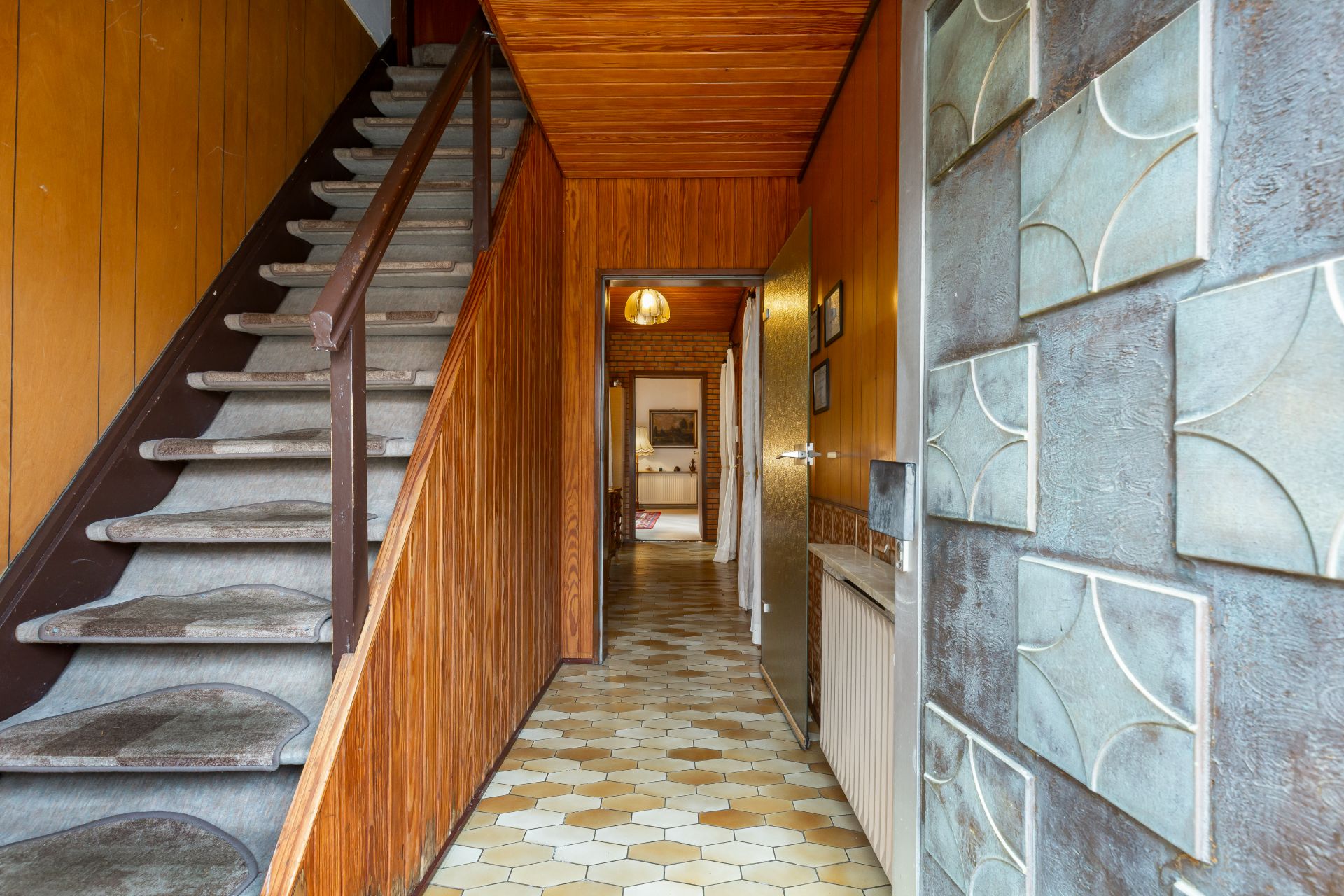 Eingangsbereich mit Holztreppe, Fliesenboden und Holzvertäfelung an den Wänden.