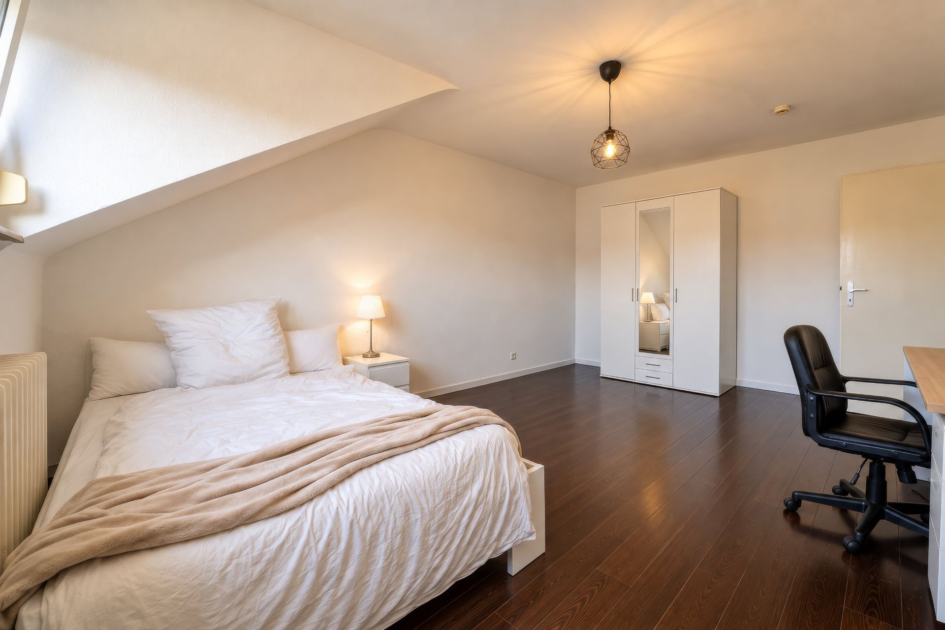 Helles Schlafzimmer mit Doppelbett, Schreibtisch, Stuhl, Kleiderschrank und Nachttischlampe.