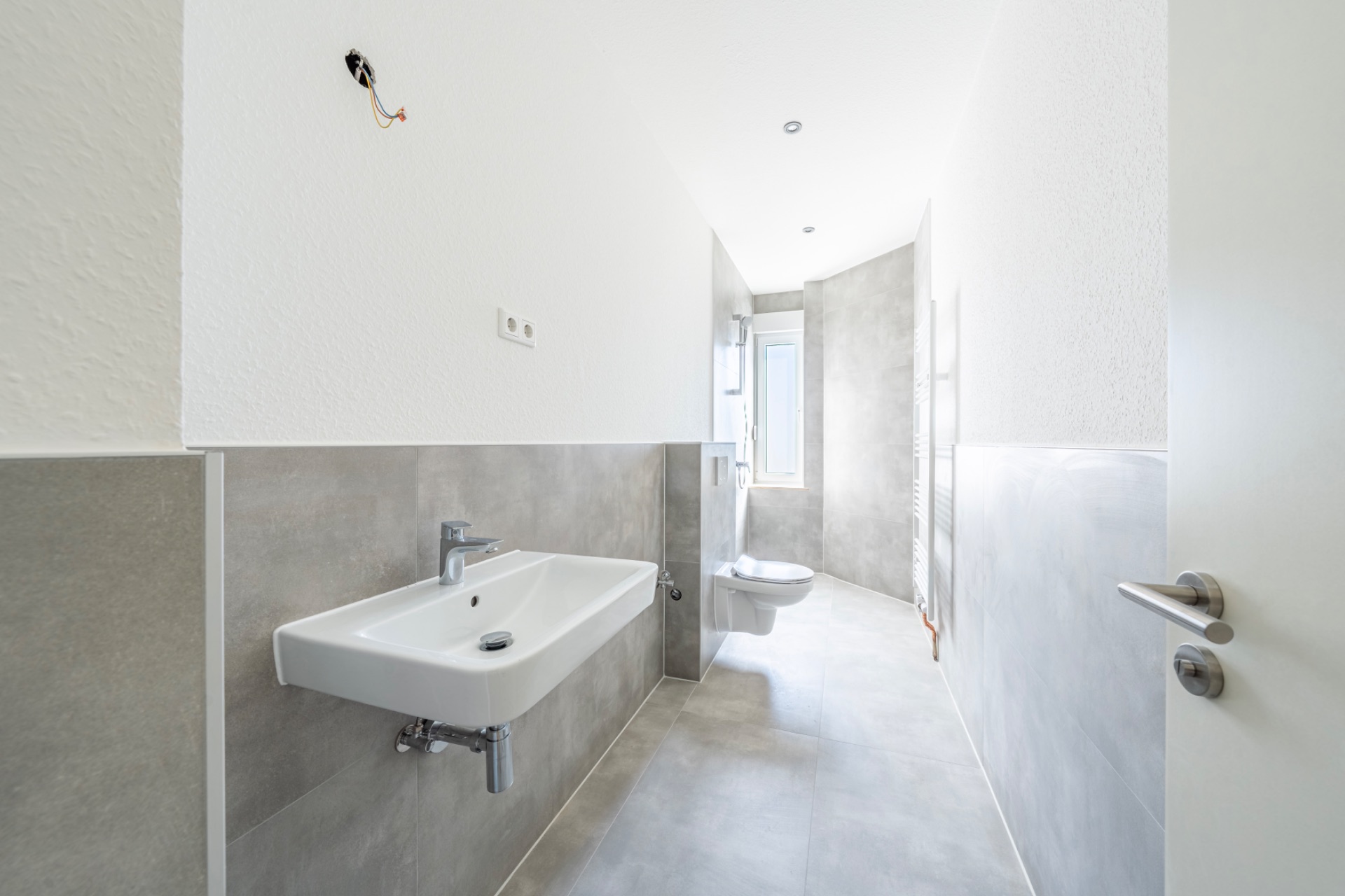 Helles, modernes Badezimmer mit Waschbecken, WC und Fenster am Ende des Raums.