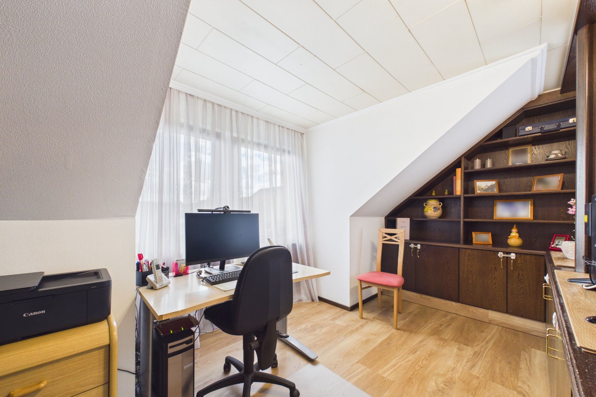 Helles Arbeitszimmer mit Schreibtisch, Computer, Regalwand und Dachschräge.