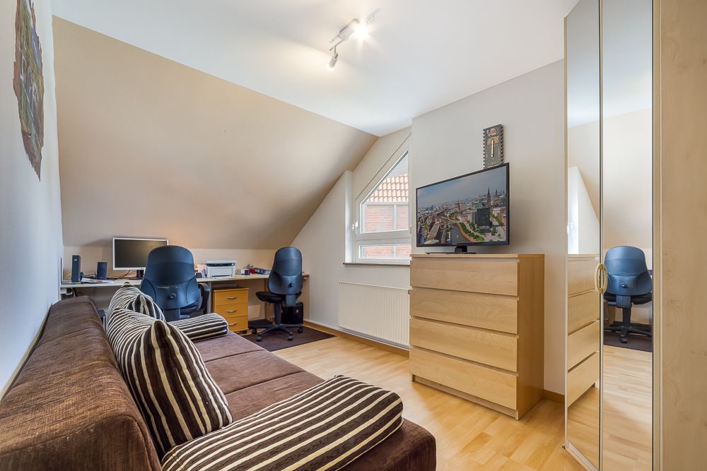 Helles Arbeitszimmer mit Sofa, Schreibtischen, Stühlen, Fernseher und Kommode unter Dachschräge.