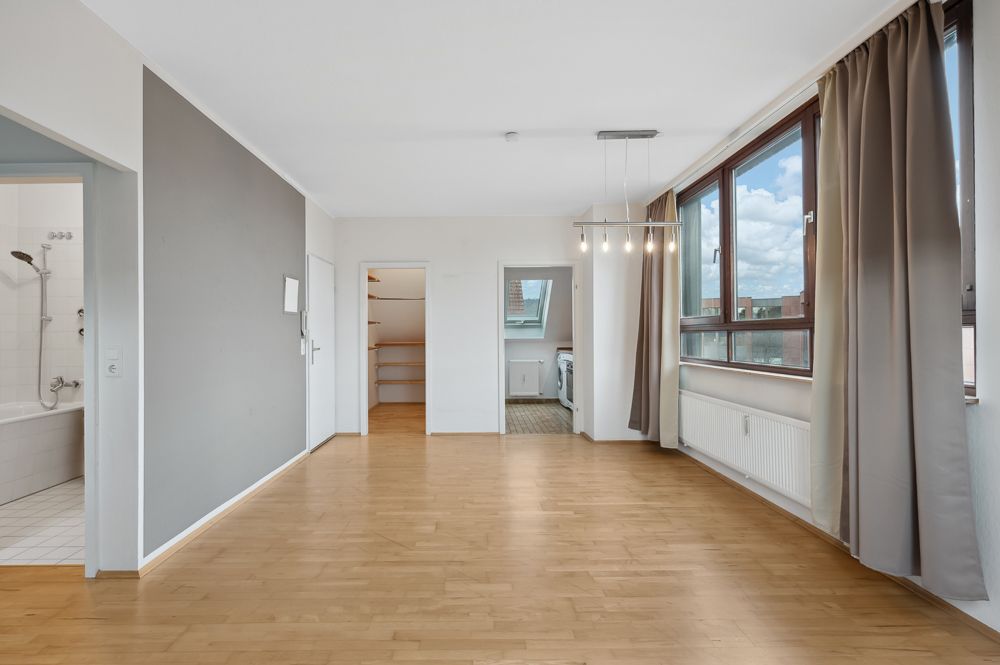 Helles Wohnzimmer mit Holzboden, großen Fenstern, Blick auf Badezimmer, Küche und Abstellraum.