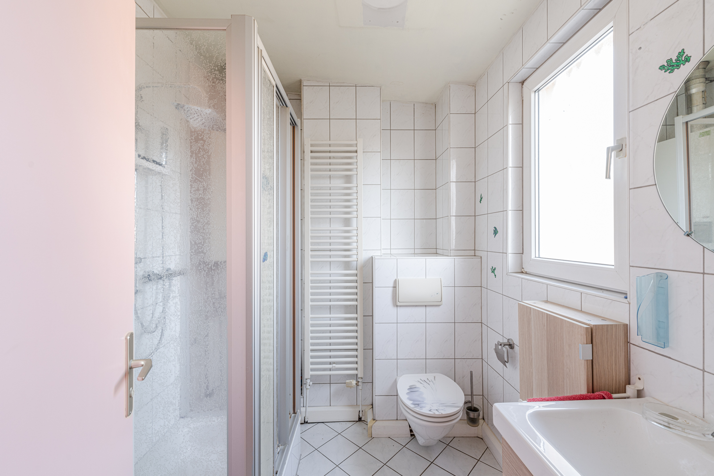Helles Badezimmer mit Dusche, Toilette, Waschbecken, Fenster und Handtuchheizkörper.