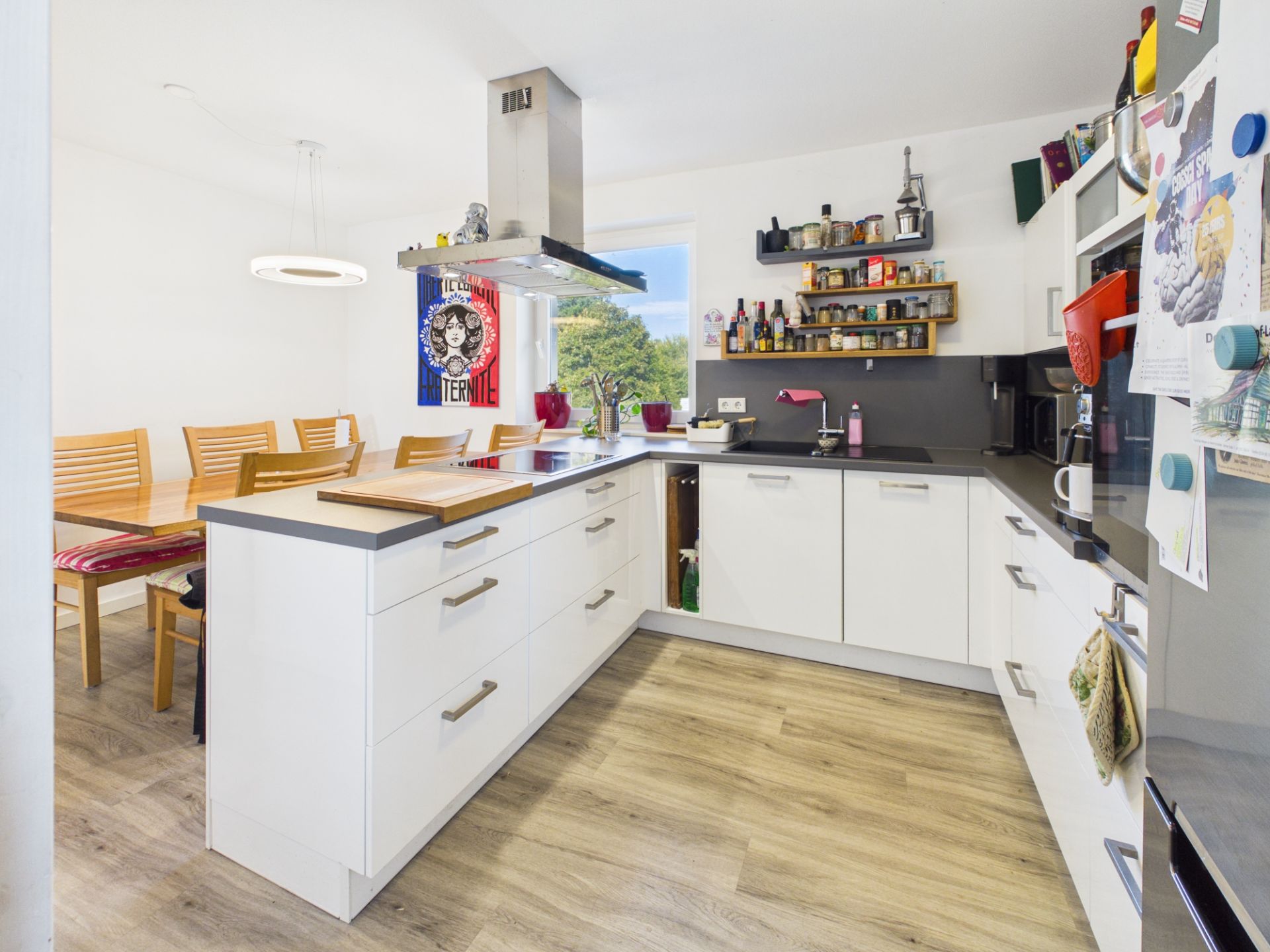 Moderne weiße Küche mit Essbereich, Holzboden und vielen Regalen an der Wand.