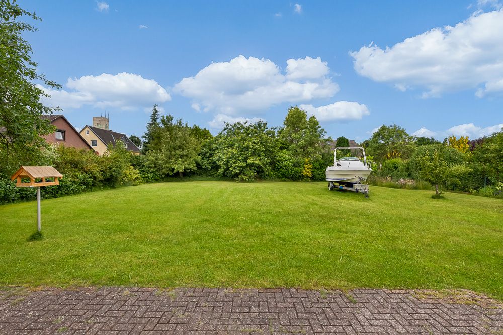 Großer grüner Garten mit einem Boot auf Anhänger und Vogelhaus, umgeben von Bäumen und Sträuchern.