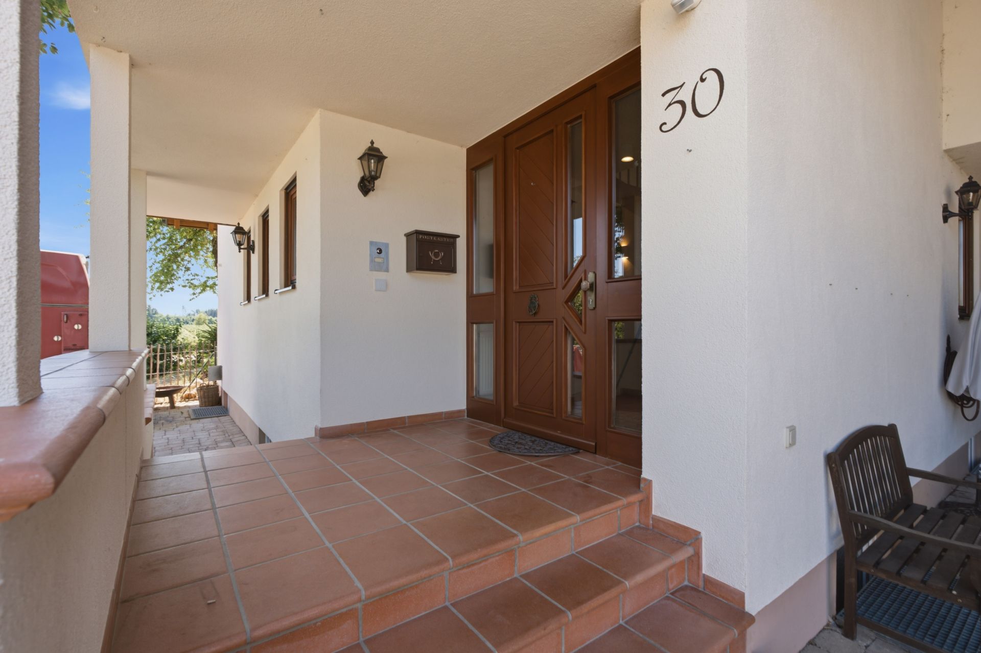 Eingangsbereich eines Hauses mit brauner Tür, Hausnummer 30 und gefliestem Boden.