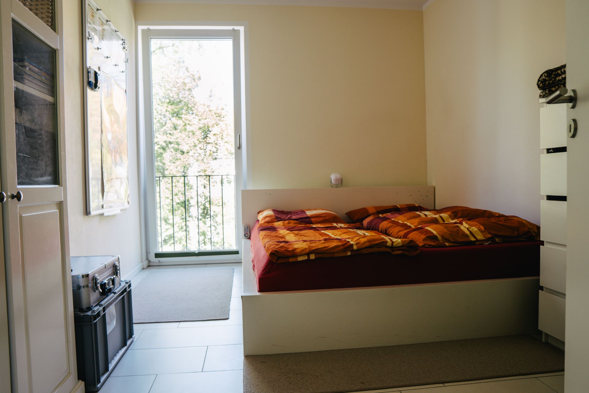 Kleines Schlafzimmer mit Doppelbett, heller Wand und Fenstertür mit Blick ins Grüne.