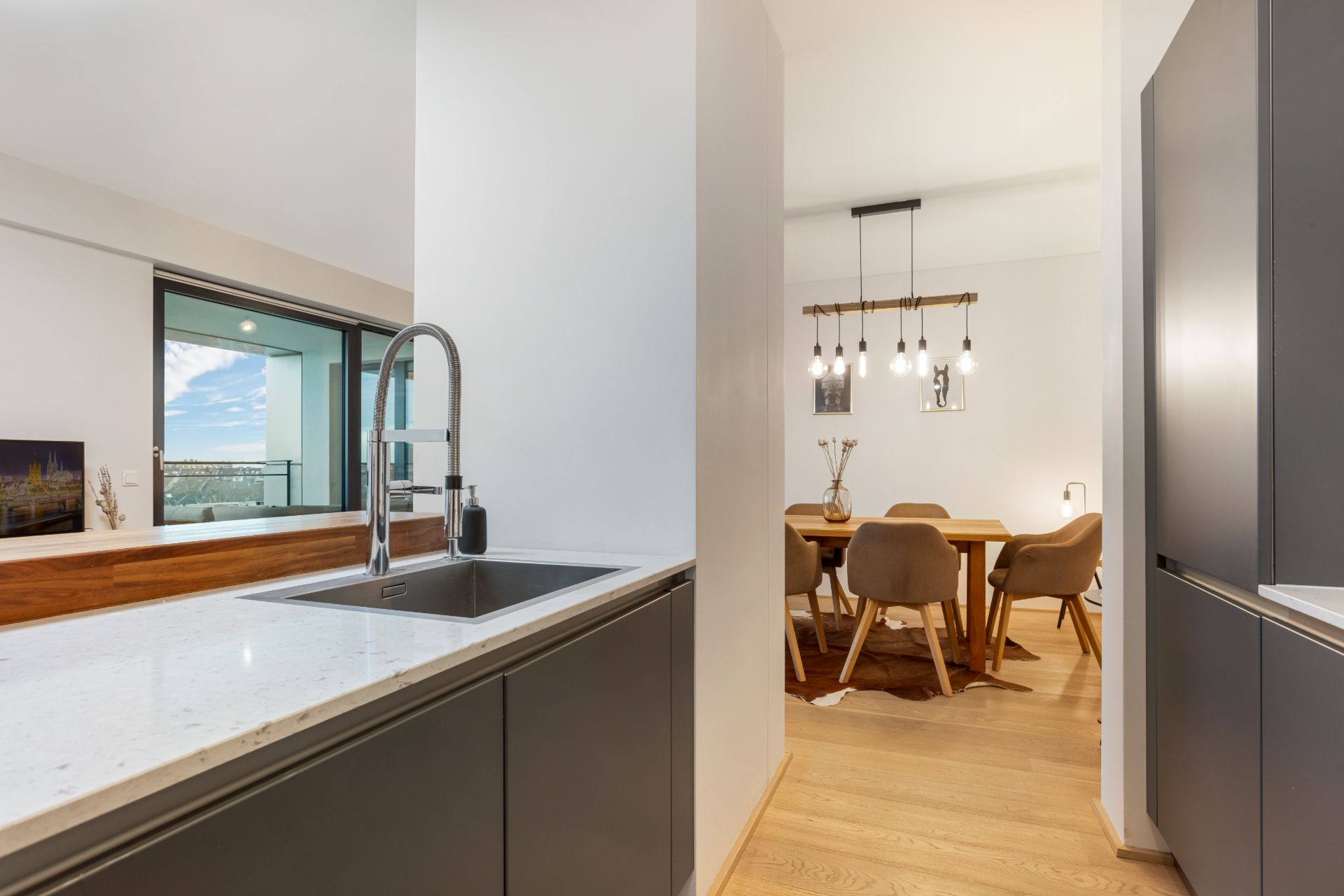 Moderne Küche mit Spüle, Essbereich mit Holztisch und Stühlen, große Fenster mit Ausblick.