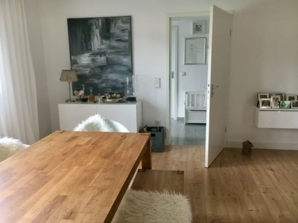 Esszimmer mit Holztisch, Stühlen mit Fellbezügen und offener Tür zu einem Flur.