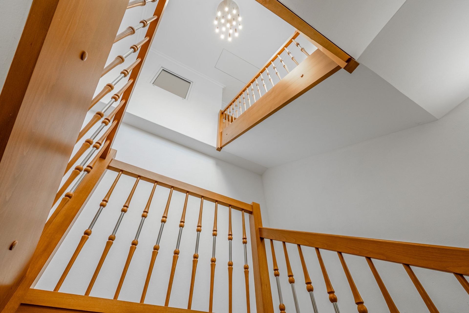 Treppe mit Holzgeländer und Lampe an weißer Decke, Blick nach oben.