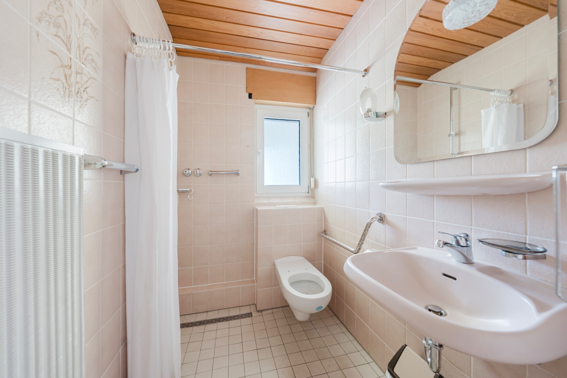 Helles Badezimmer mit WC, Waschbecken, Dusche mit Vorhang und Fenster.