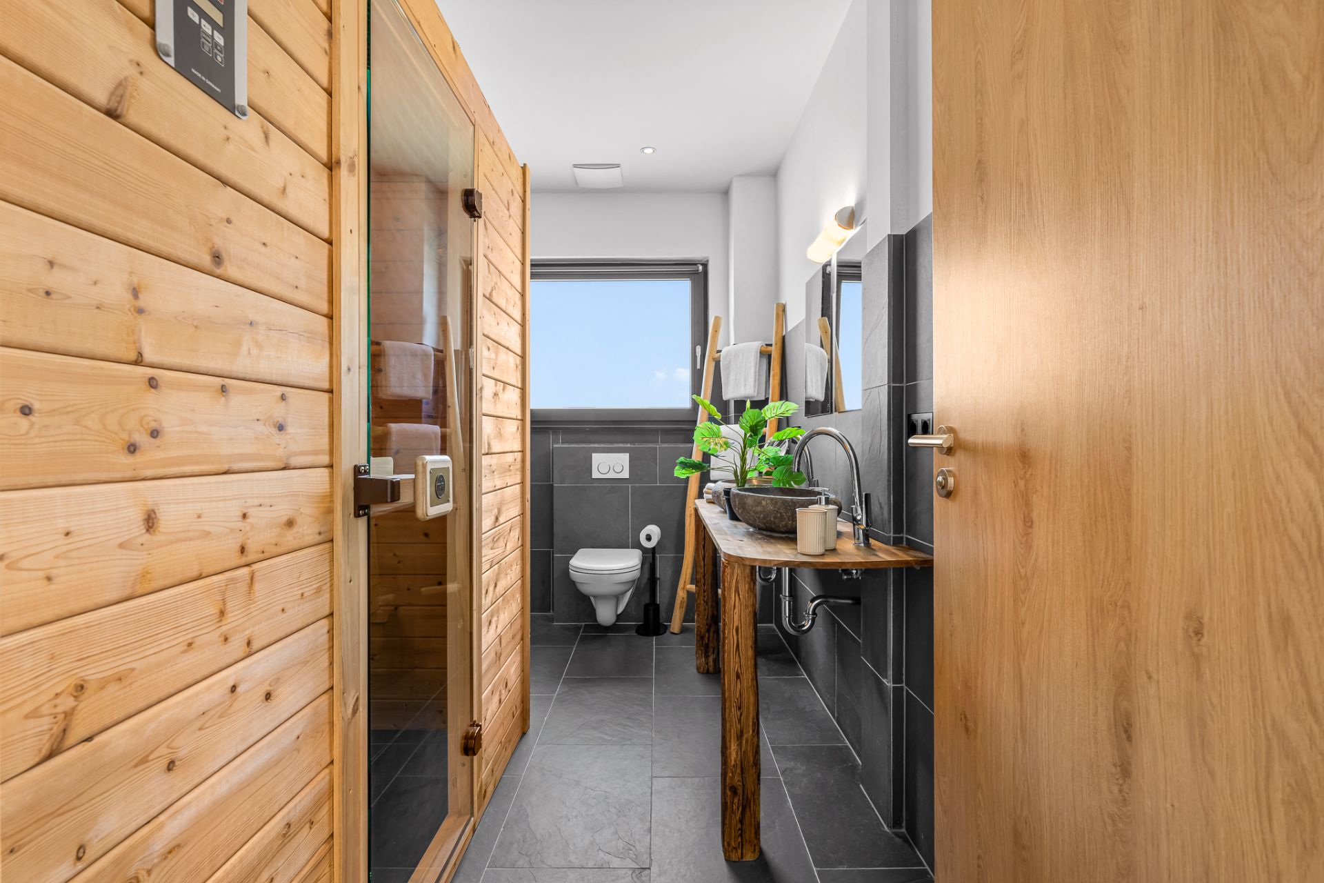 Modernes Badezimmer mit Holzsauna, Toilette, Waschbecken und großem Fenster.