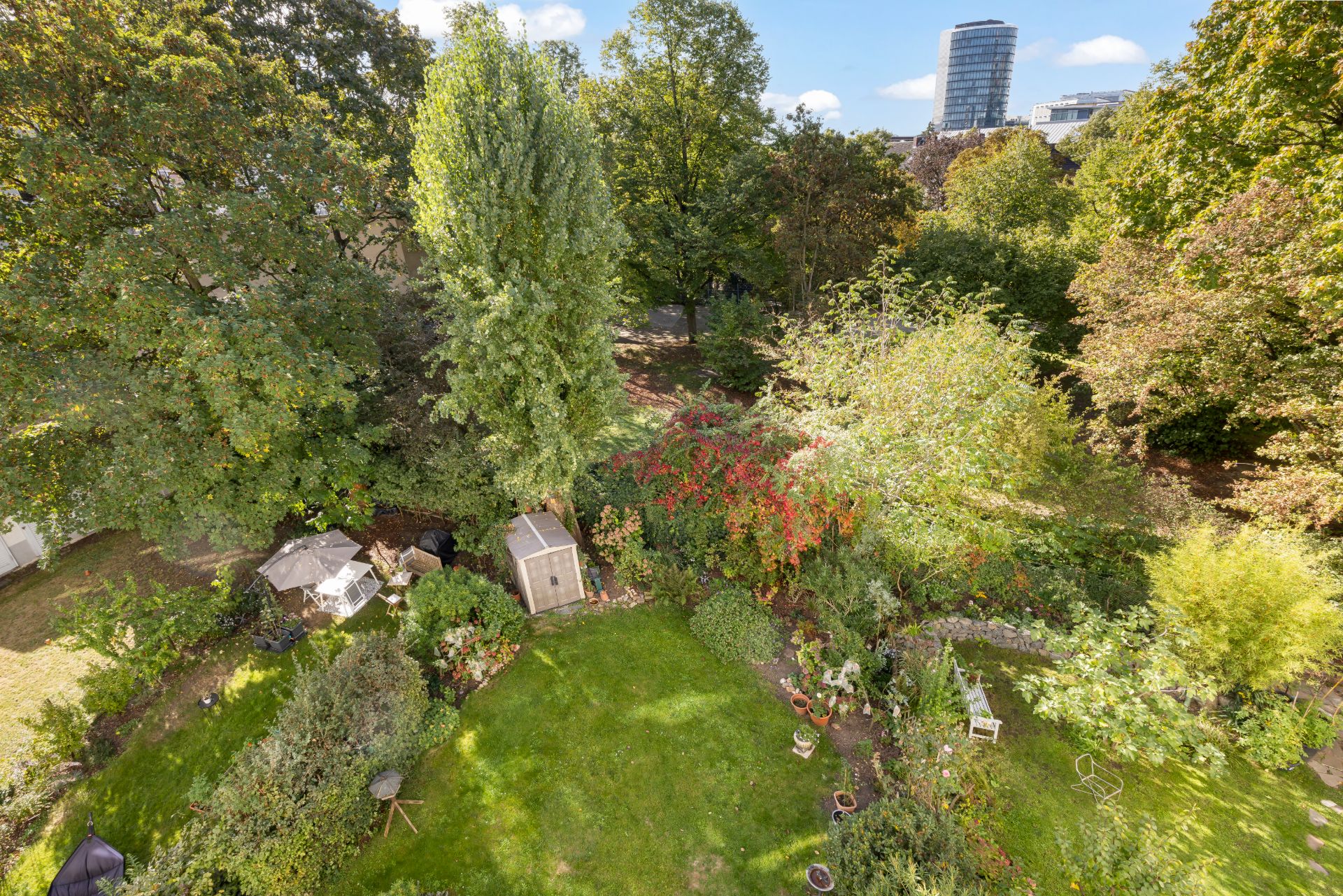 Großer Garten mit Rasenfläche, Bäumen, Sträuchern, Gartenhaus und Sitzgelegenheiten.