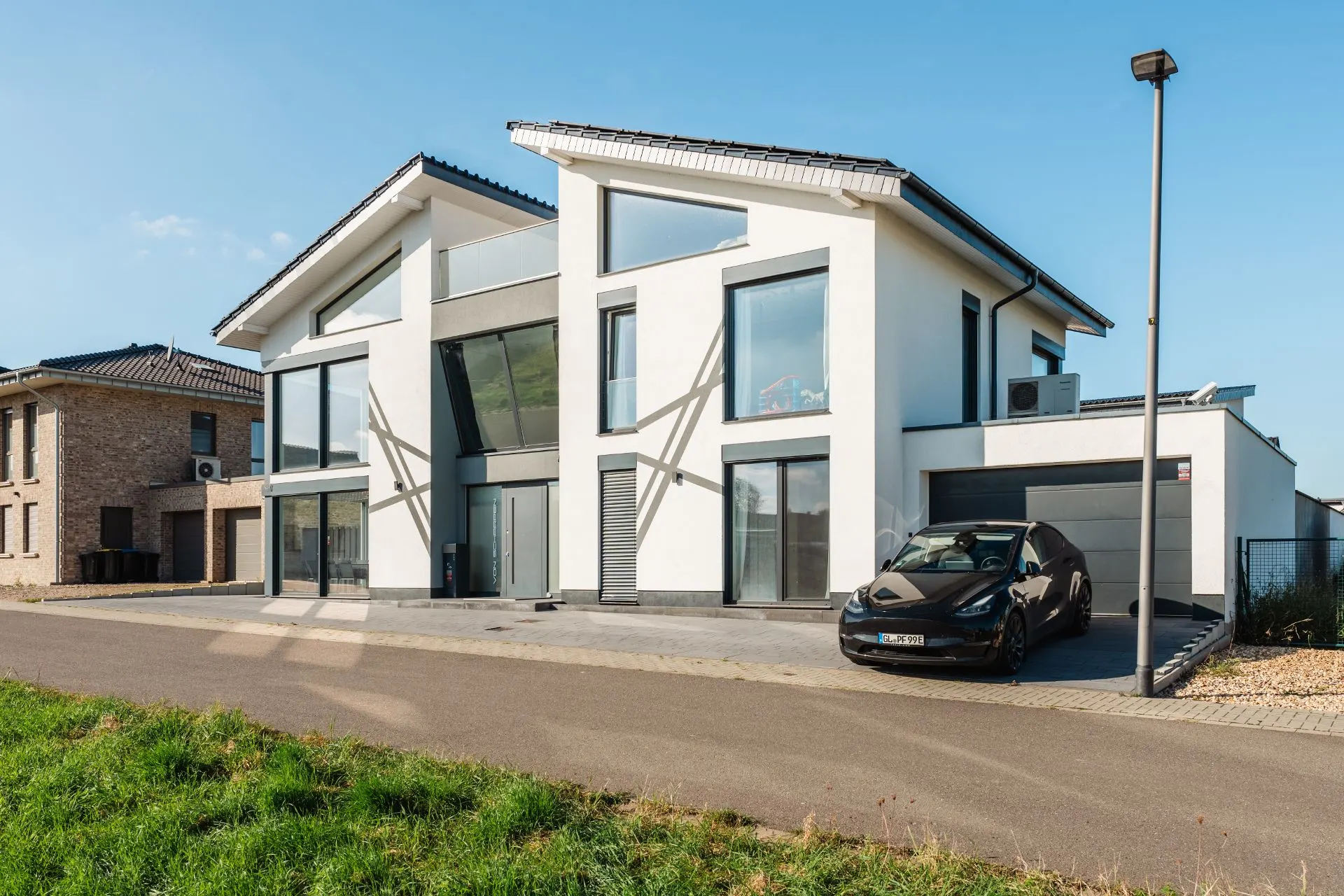 Modernes weißes Wohnhaus mit großen Fenstern und schwarzem Auto vor der Garage.
