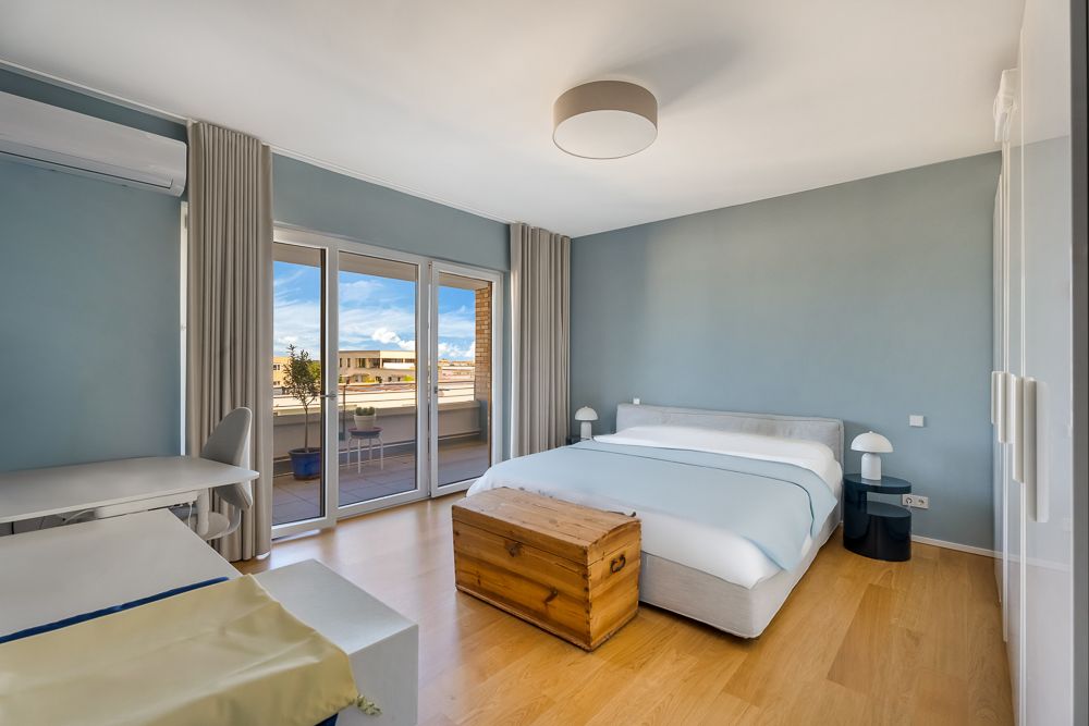 Helles Schlafzimmer mit Doppelbett, Holzboden und Zugang zu einer Terrasse durch große Glastüren.