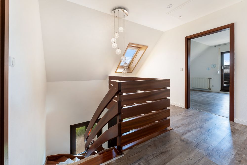 Heller Flur mit Holztreppe, Dachfenster und modernem Kronleuchter.