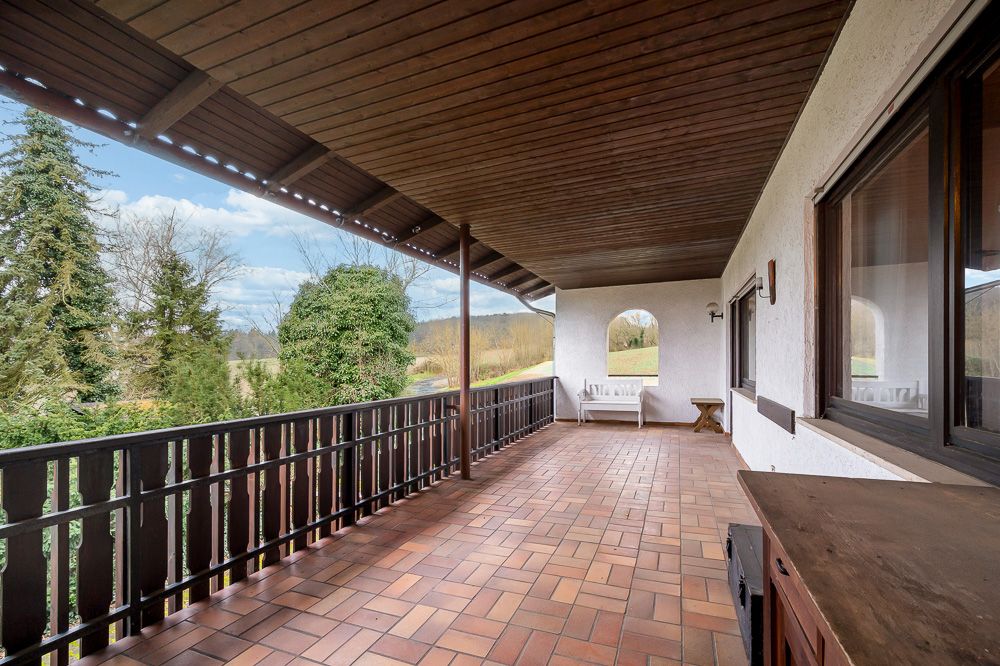 Überdachte Terrasse mit Fliesenboden, Holzzaun und Blick ins Grüne.