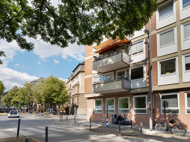 Eckwohnhaus mit Balkonen und großen Fenstern an einer Straßenecke, daneben geparkte Fahrräder.
