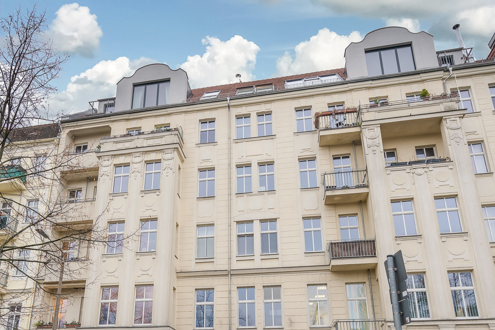 Mehrstöckiges Wohngebäude mit Balkonen und großen Fenstern, helle Fassade bei Tageslicht.