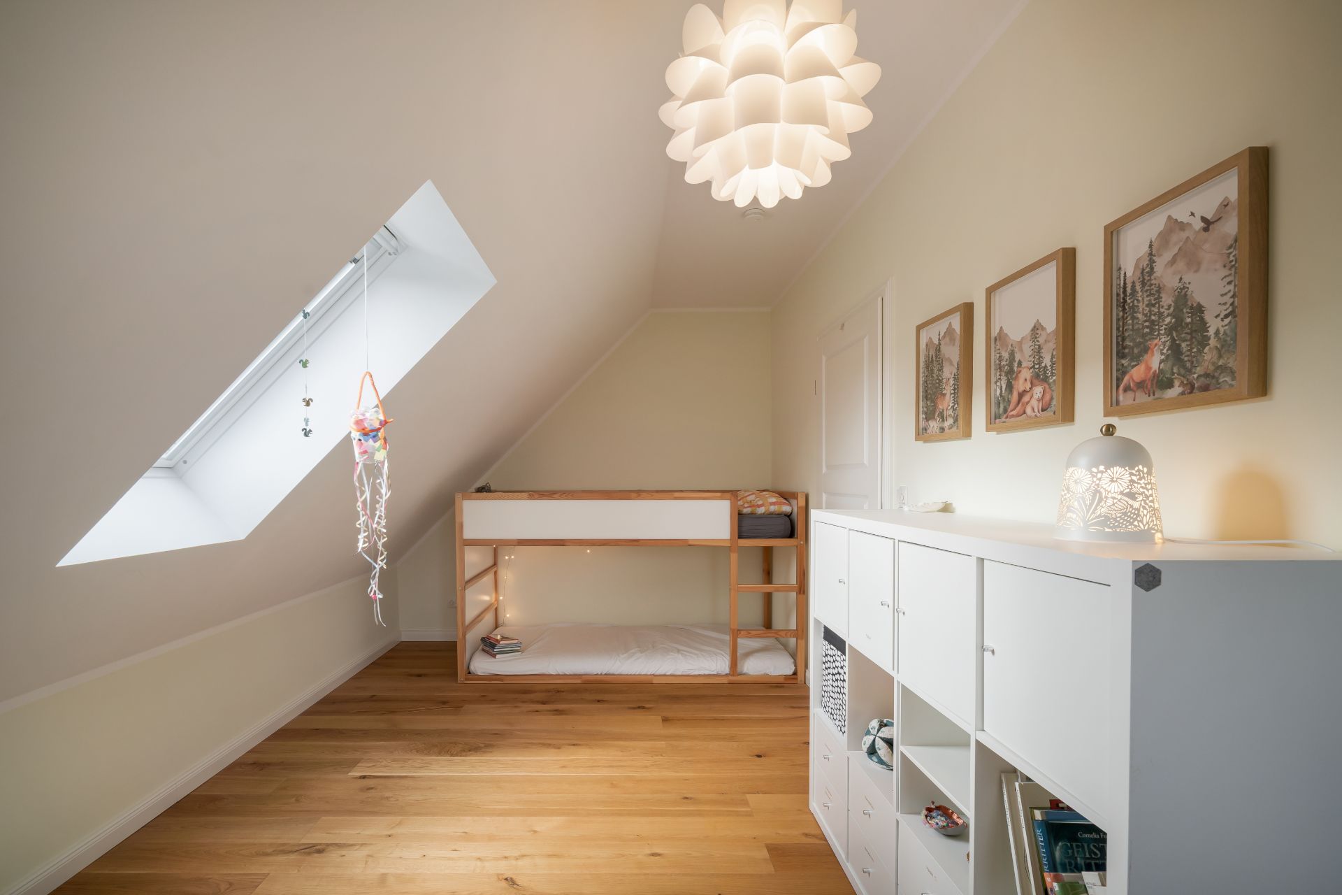 Helles Kinderzimmer mit Hochbett, Holzboden, Dachfenster und weißem Regal.