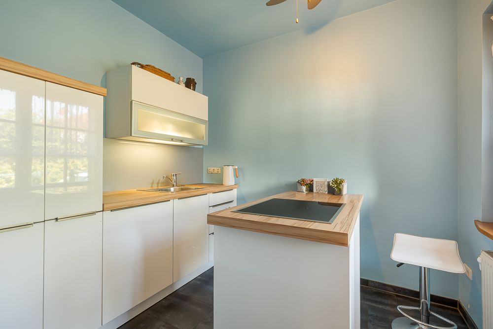 Moderne Küche mit hellen Schränken, Kochinsel und Barhocker vor blauer Wand.