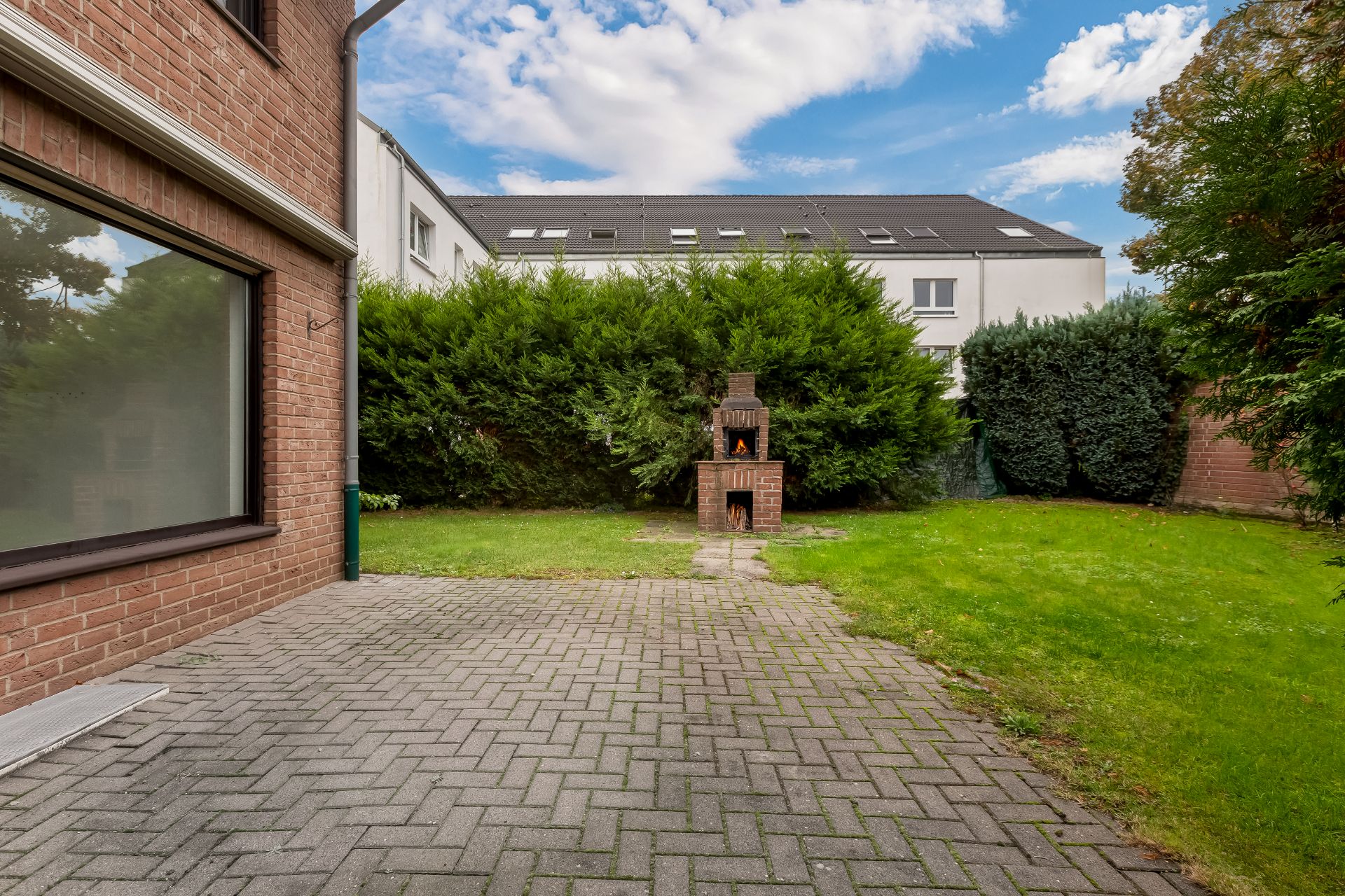 Gepflasterte Terrasse mit gemauertem Grill und angrenzendem Rasen im Garten.