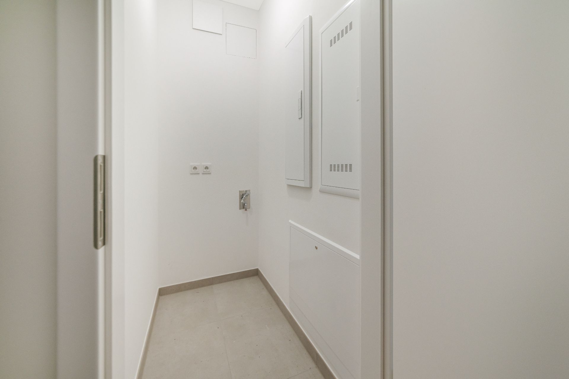 Heller, schmaler Flur mit weißen Wänden und grauem Boden, Wandpaneelen und Steckdosen.