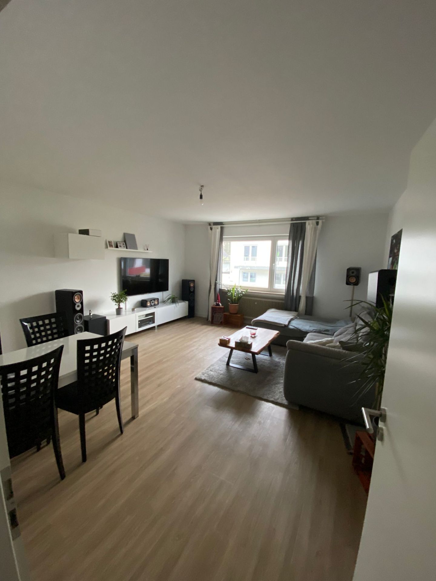 Modernes Wohnzimmer mit Sofa, Esstisch, Fernseher und großem Fenster.