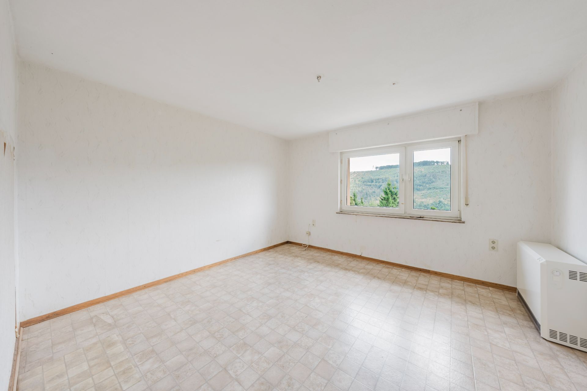 Leerer, heller Raum mit großem Fenster und Blick ins Grüne.