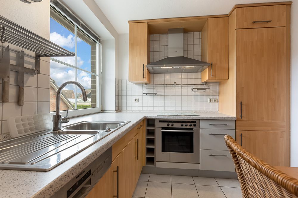 Moderne Einbauküche mit Holzfronten, Spüle, Herd, Dunstabzugshaube und großem Fenster.