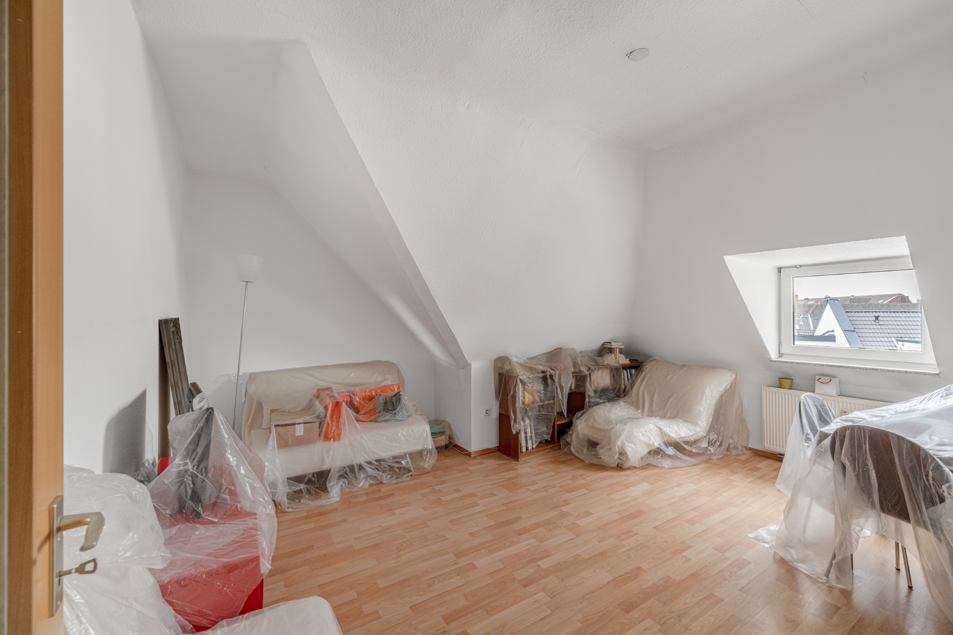 Wohnzimmer mit Möbeln, die mit Plastikfolie abgedeckt sind, und einem Fenster mit Blick nach draußen.