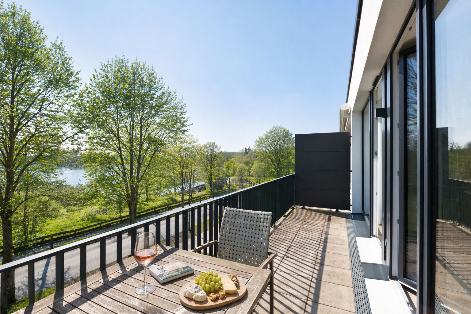 Balkon mit Tisch, Stuhl, Wein, Trauben und Blick auf grüne Bäume und einen Fluss.