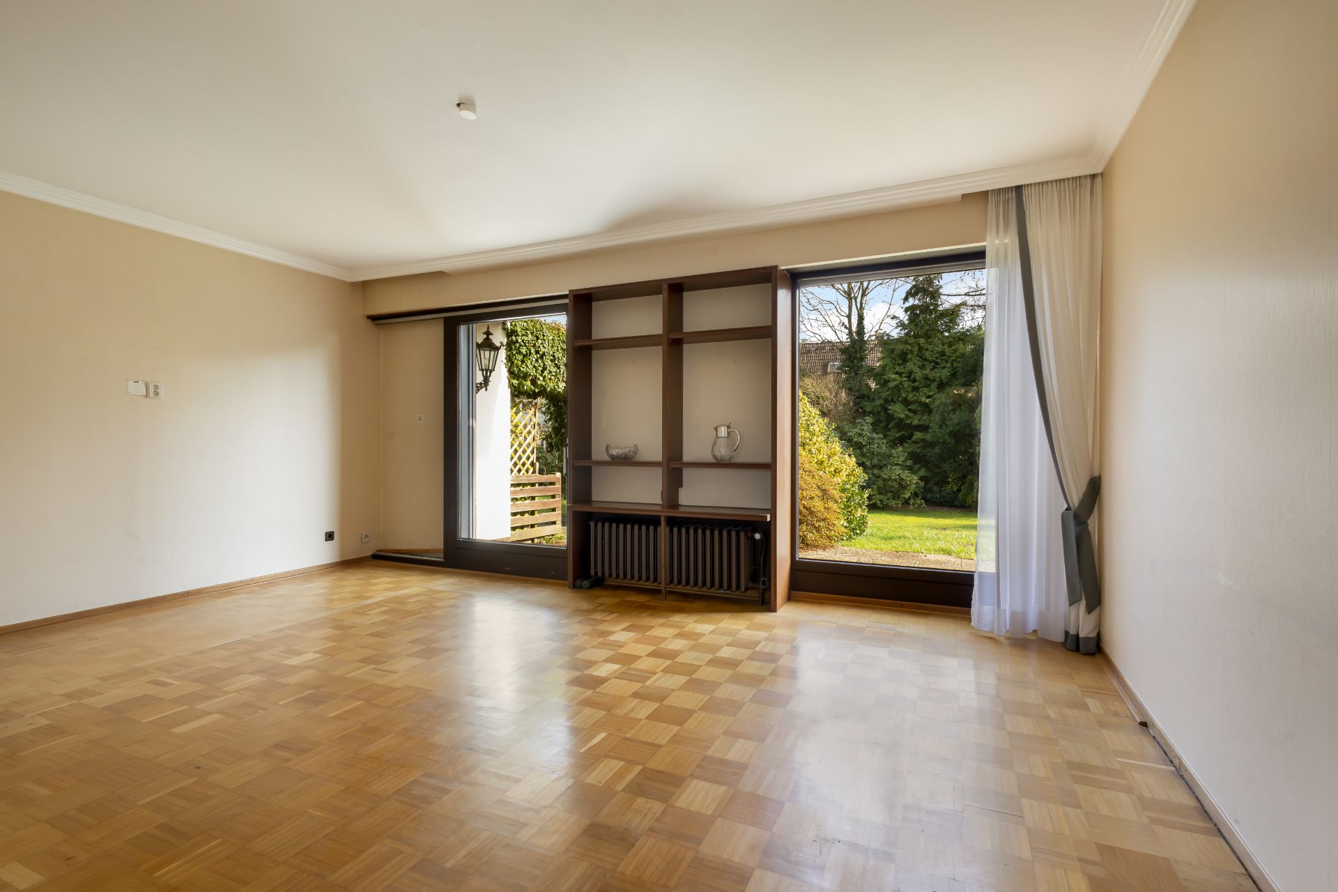 Leeres Wohnzimmer mit Parkettboden, großen Fenstern und Blick auf den Garten.