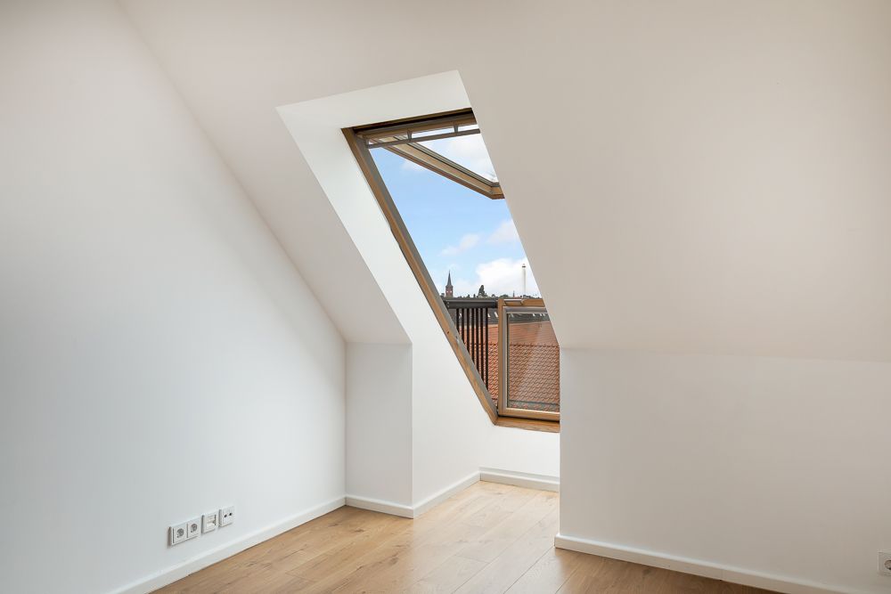 Helles Zimmer mit schräger Decke, großem Dachfenster und Holzboden.
