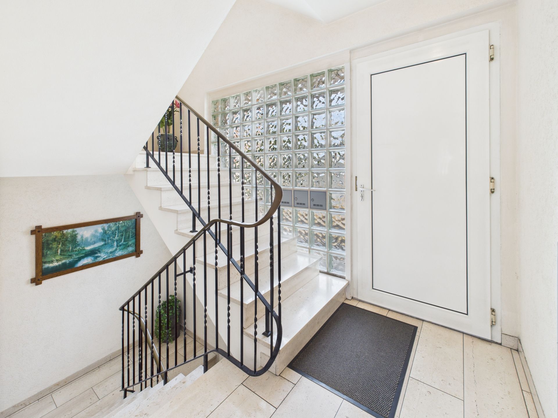 Heller Eingangsbereich mit weißer Tür, Glaselementen, Treppe und Gemälde an der Wand.