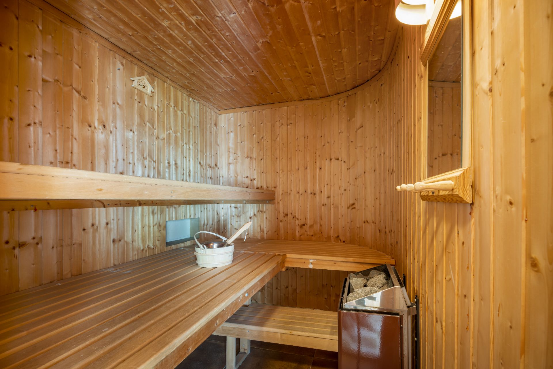 Holzsauna mit Bänken, Saunaofen, Eimer und Schöpfkelle.
