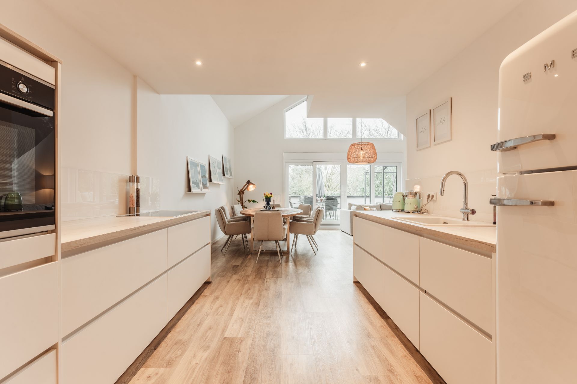 Helle, moderne Küche mit Essbereich, Holzboden und großen Fenstern im Hintergrund.