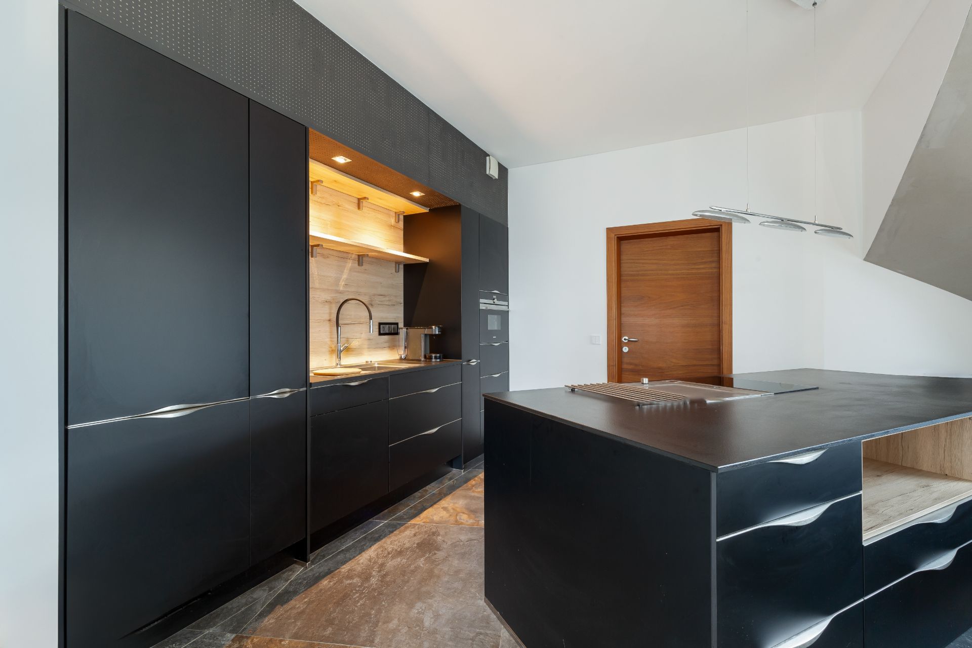 Moderne Küche mit schwarzen Schränken, Kochinsel und Holztür im Hintergrund.