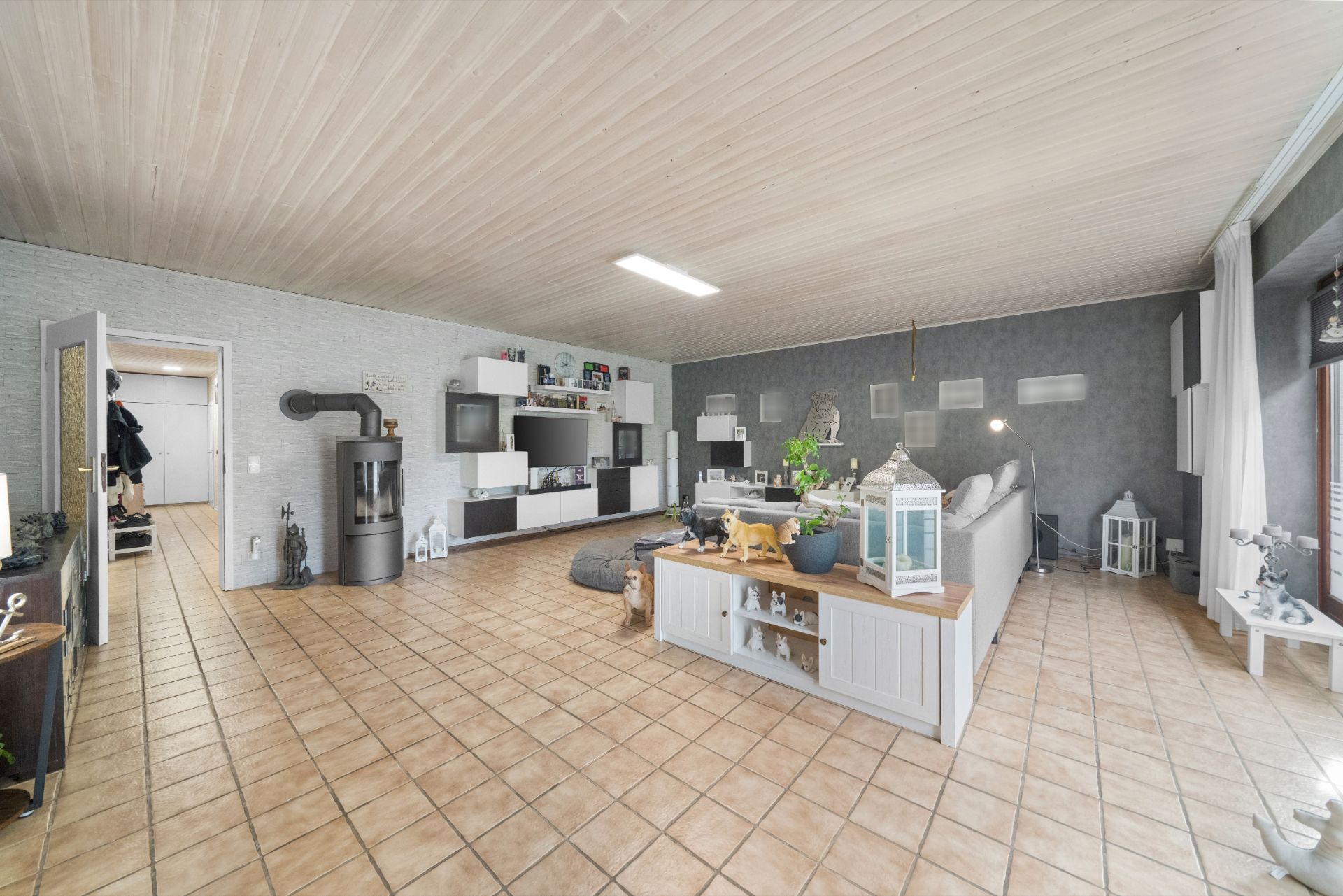 Helles Wohnzimmer mit Fliesenboden, Kaminofen, Sofa und Regalwand.