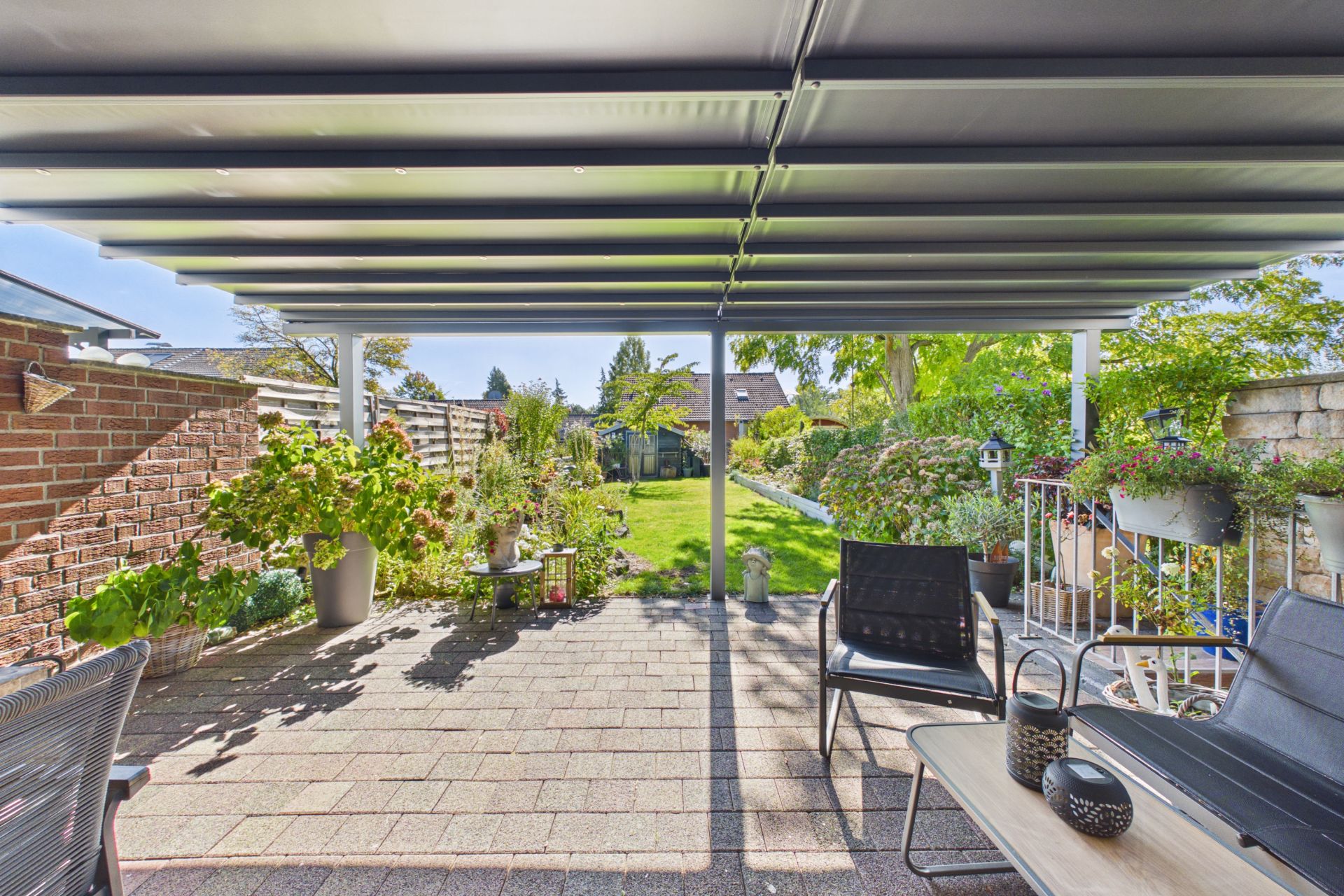 Überdachte Terrasse mit Gartenmöbeln und Blick auf einen bepflanzten Garten.