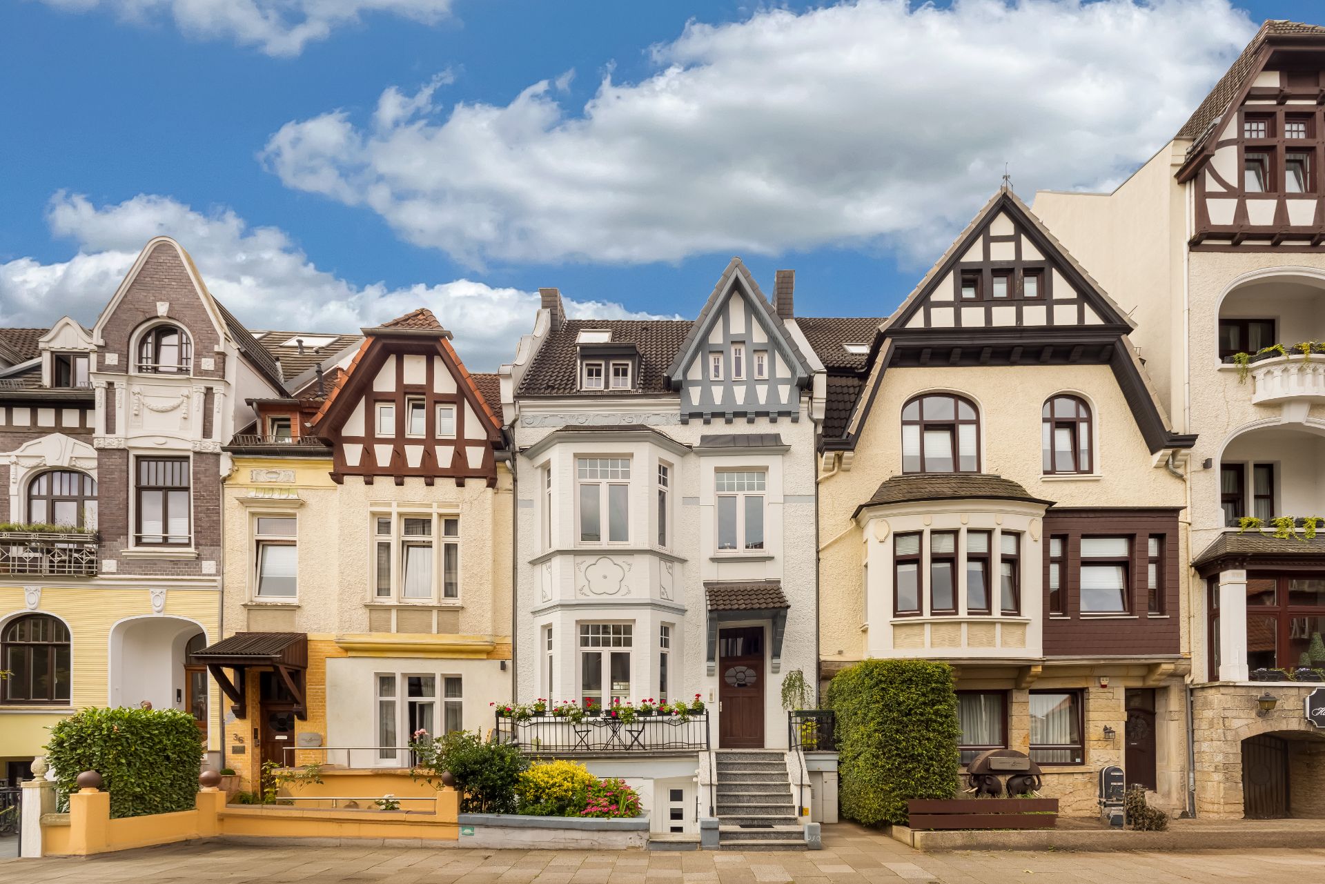 Historische Wohnhäuser mit Erkern und Fachwerkelementen an einer Straße bei blauem Himmel.