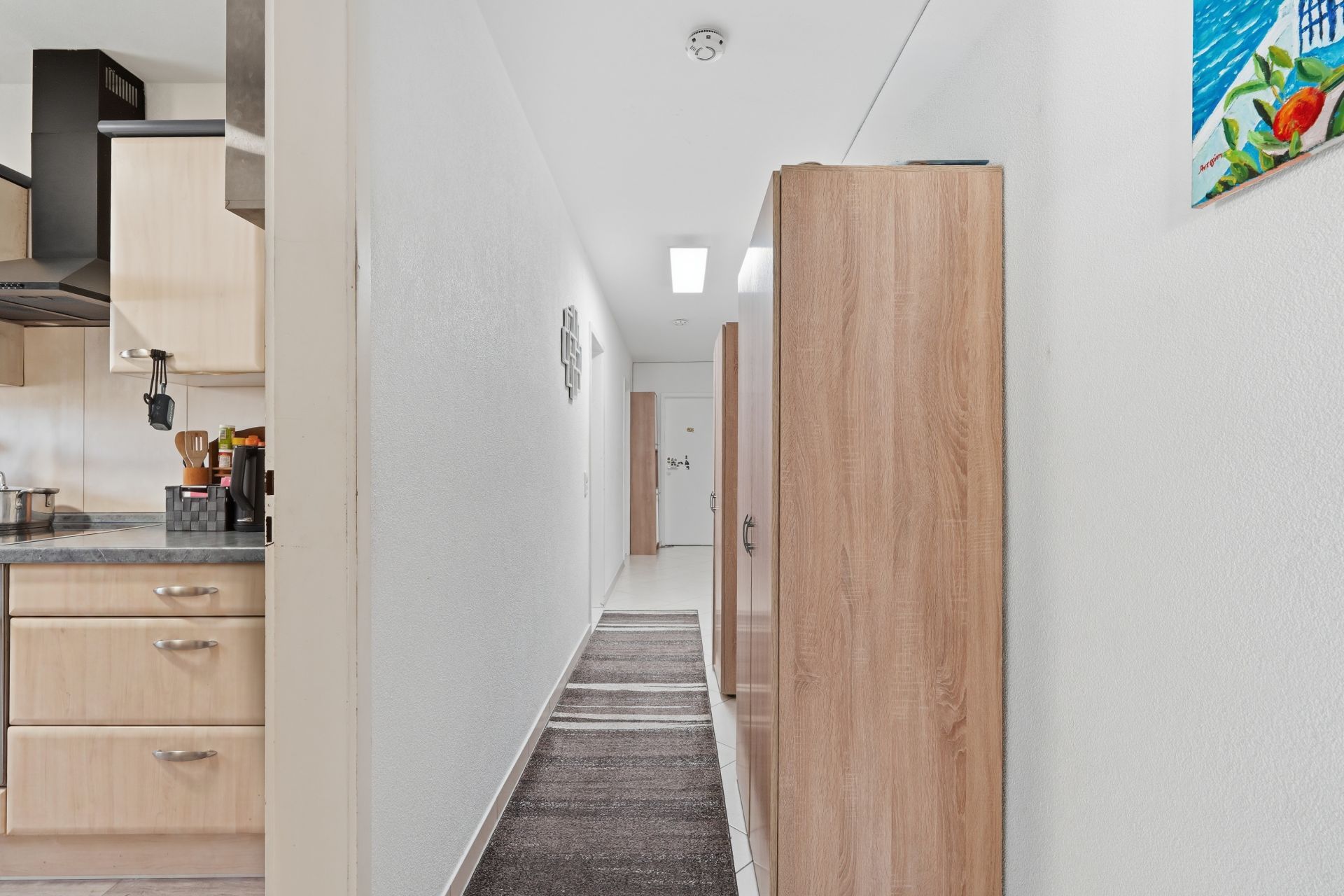 Heller Flur mit Teppich, Holzschränken und Blick in eine Küche mit Holzmöbeln.