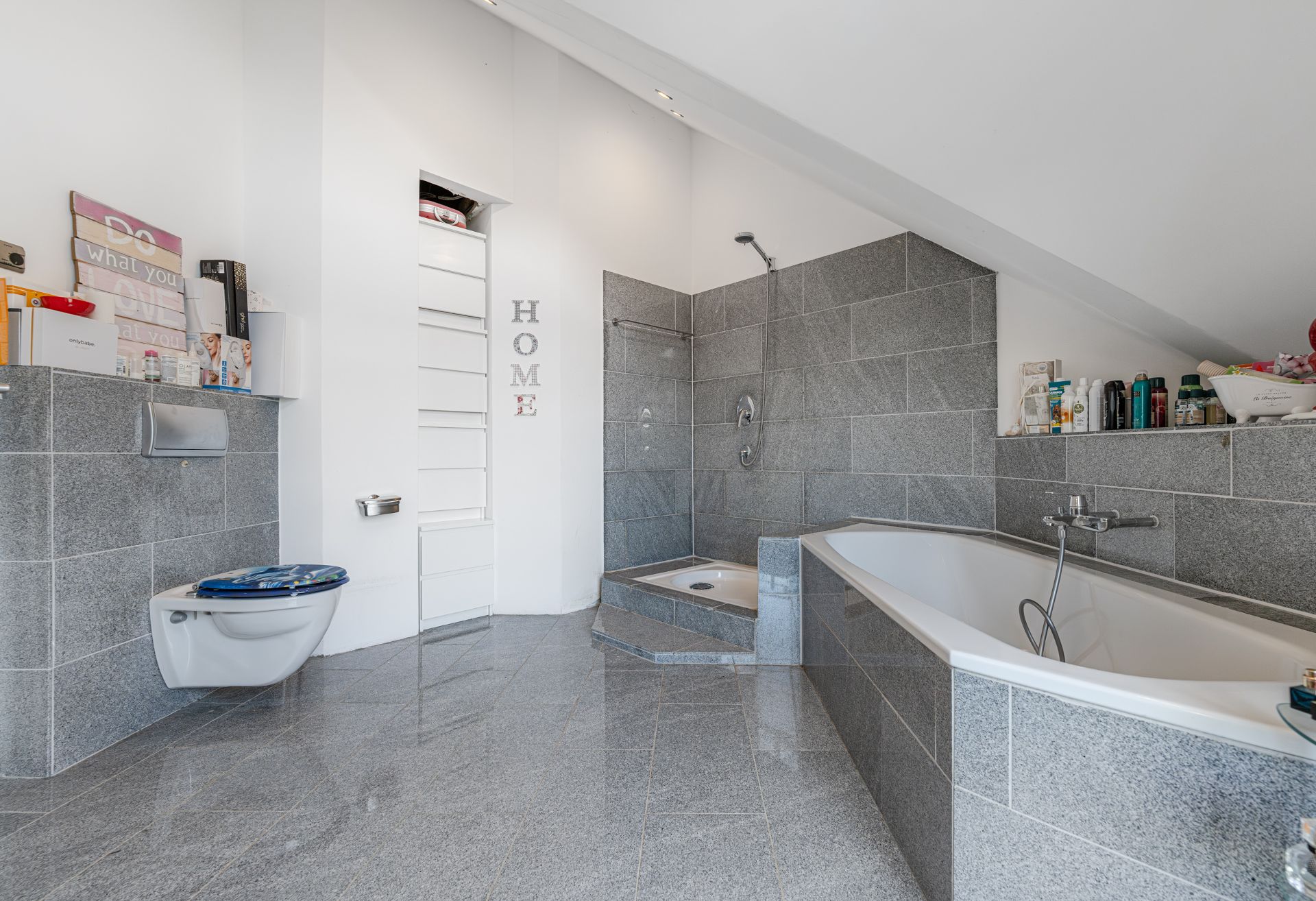 Modernes Badezimmer mit Badewanne, Dusche und Wandtoilette unter einer Dachschräge.